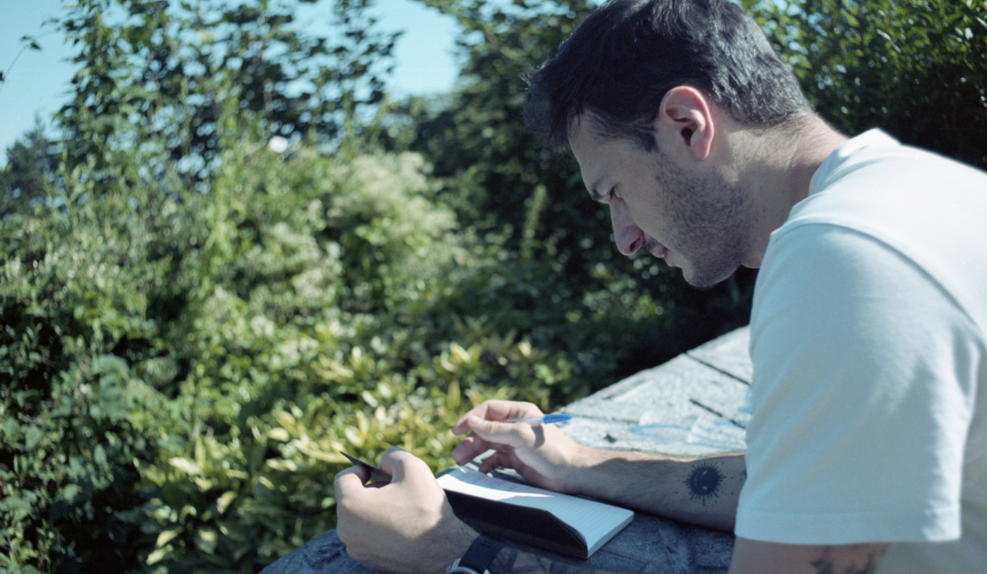 jeremy écrit dans un journal de bord avec la nature en fond